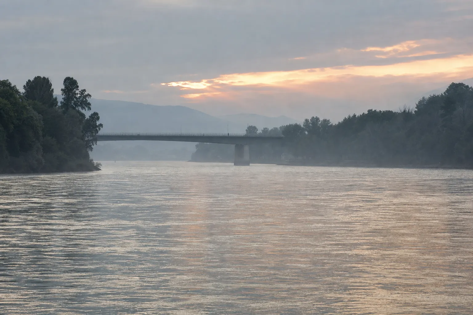 Pont routier discret enjambant le Rhin en fin d’après-midi, brume légère sur l’eau