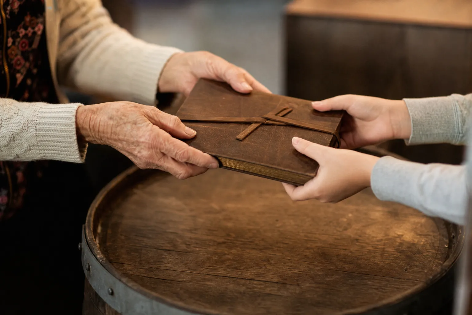 Deux paires de mains se passant un carnet de famille relié en cuir au-dessus d’une table